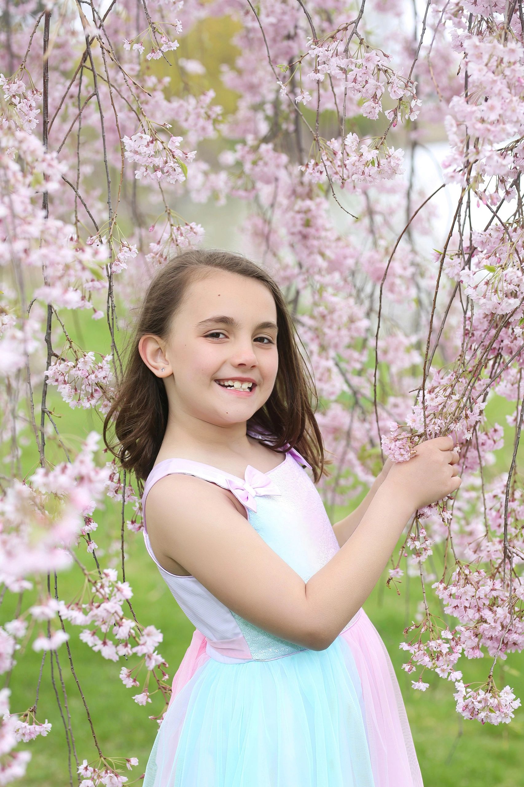 Young girl smiling among pink cherry blossoms outdoors.