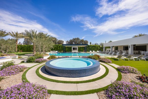 Modern backyard with a circular hot tub, pool, and lounge chairs under a blue sky.