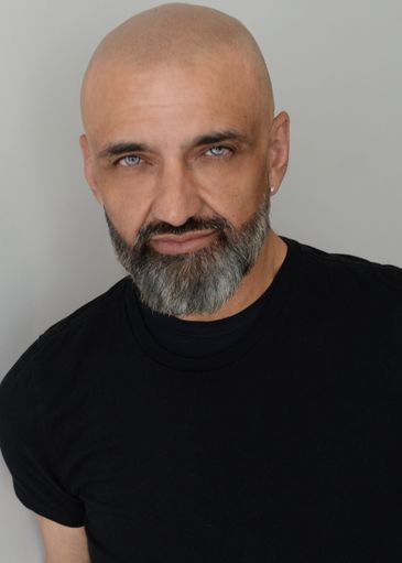 Bald man with a gray beard wearing a black t-shirt against a plain background.
