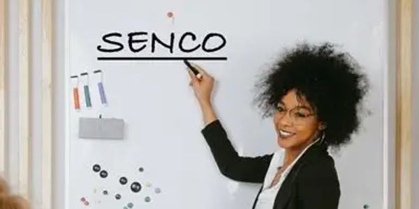 Woman smiling while pointing to the word SENCO on a whiteboard.