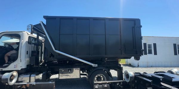 A white truck with a large black container bed under clear blue sky.