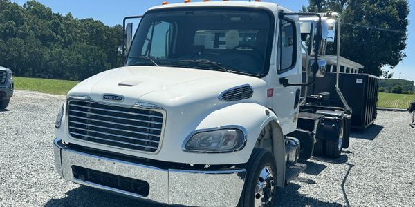 White Freightliner truck with a trailer on a gravel lot on a sunny day.