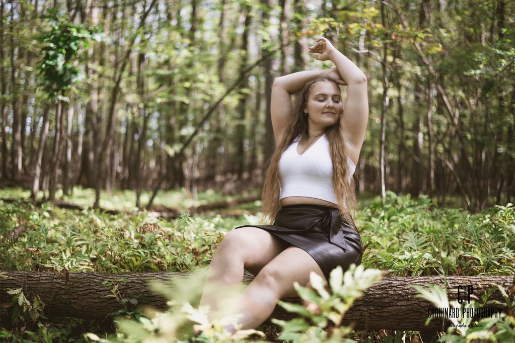 Une jeune femme assise sur un tronc,  en forêt. Elle fais la pose pour la photo.