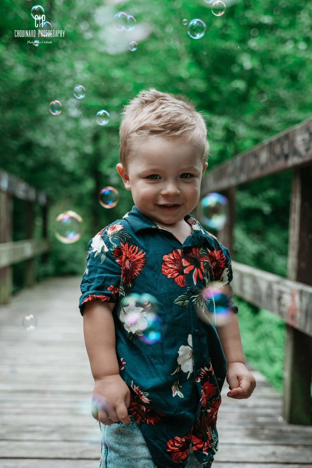 Un enfant souriant, sur un pont de bois. Il a y des bulles de savon dans l'air.