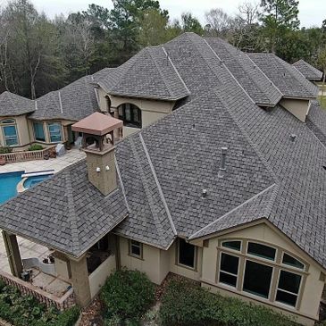 A large house with a complex gray shingled roof and a swimming pool.