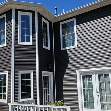 Modern dark gray house exterior with white-trimmed windows and doors under clear blue sky.