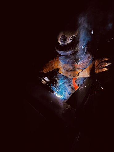 Welder working with bright sparks and smoke in dark surroundings.