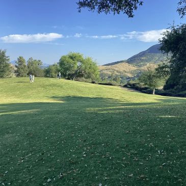 Two people walking on a grassy hill with trees and mountains in the background.