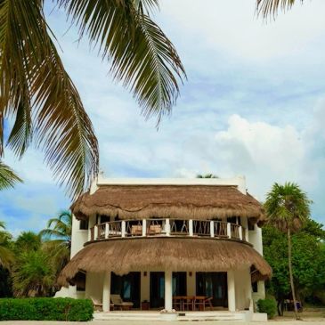Tropical two-story beach house with thatched roof.