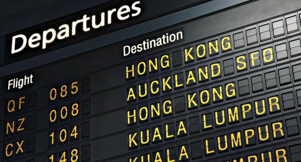 A close-up of an airport departure board showing destinations like Hong Kong and Auckland.
