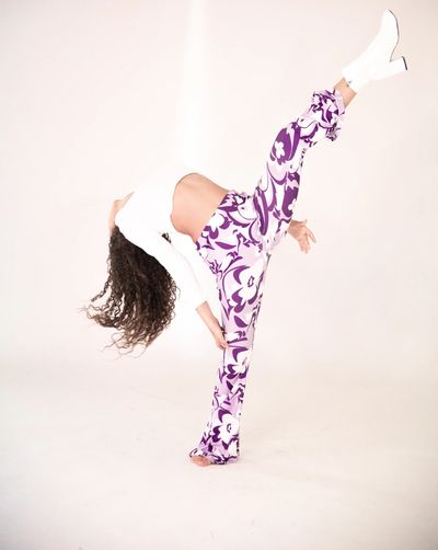 Woman in floral pants performing a high kick against a white background.