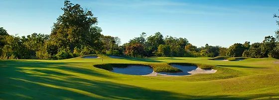 Scenic golf course with sand bunkers and lush green fairways under a clear sky.