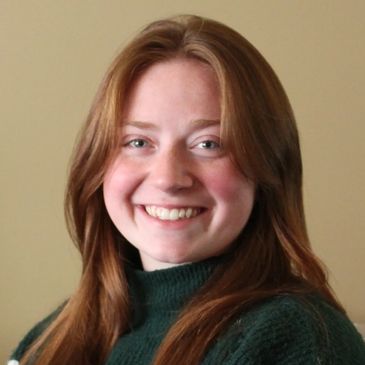 A headshot of a woman smiling with long brownish red hair and a green turtleneck shirt