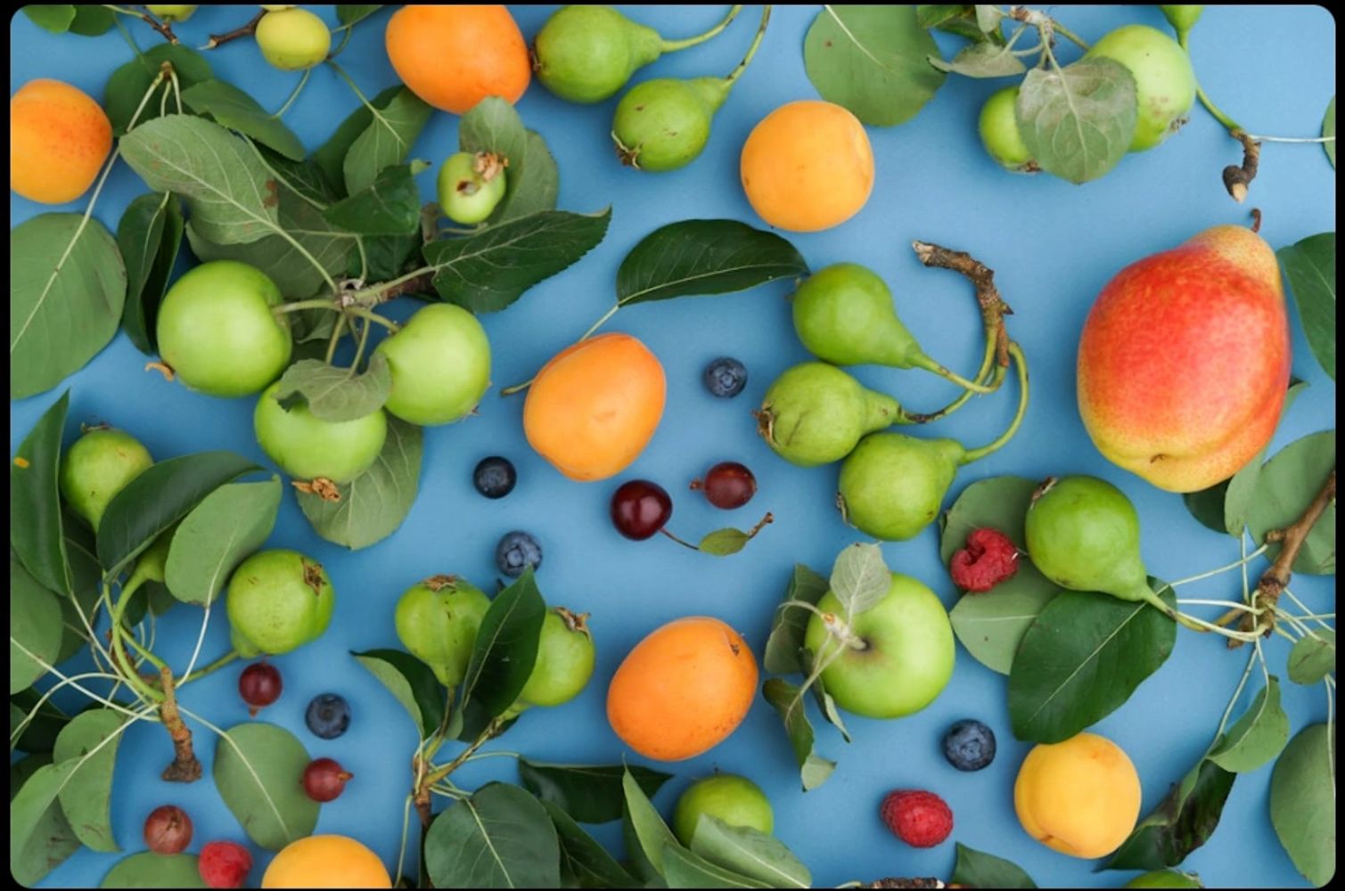 Assorted fresh fruits and green leaves on a blue background.