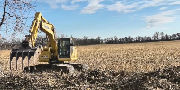 Yellow excavator with claw attachment working in a field under blue sky.