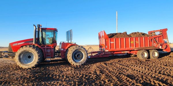Red tractor pulling a loaded red trailer on a dirt field under a clear blue sky.