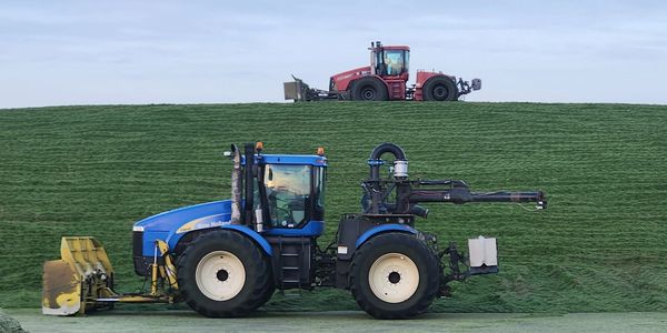 Two large tractors on green grassy terrain, one blue in front and one red on a hill behind.