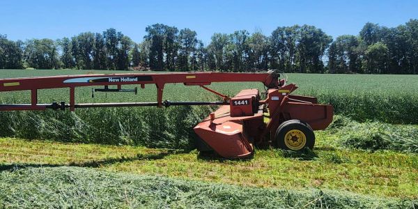A New Holland mower cutting grass in a field on a sunny day.