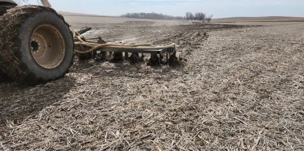 Tractor tilling a dry, bare field under a clear sky.
