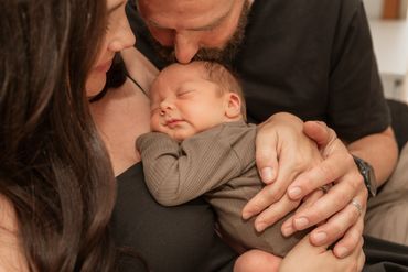 Parents lovingly cradle their peacefully sleeping newborn baby.