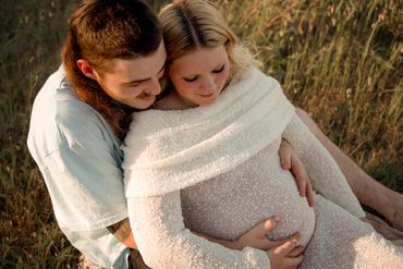 Couple embracing outdoors with the woman showing her pregnant belly.