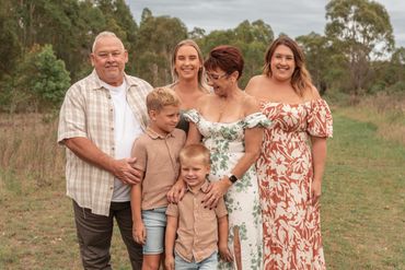 A smiling family of five posing outdoors in casual and floral attire.