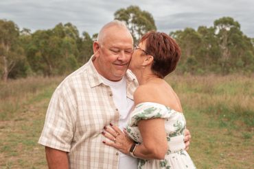 Elderly woman kissing a happy elderly man outdoors.