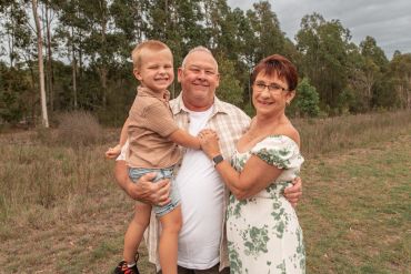 Smiling grandparents holding their grandson outdoors.