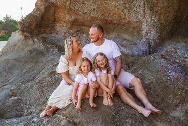 Happy family of four sitting barefoot on a rocky surface outdoors.