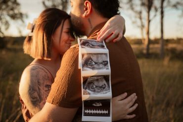 Couple hugging with ultrasound pictures at sunset.