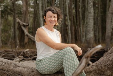 Smiling woman sitting on a large tree branch in a forest.