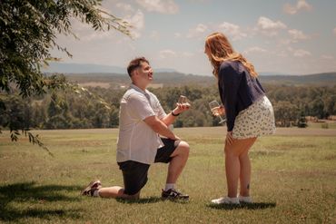Man proposes marriage outdoors to a surprised woman on a sunny day.