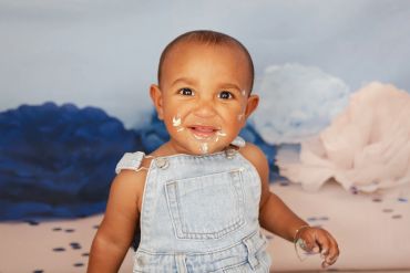 Happy baby with cake on face in denim overalls.