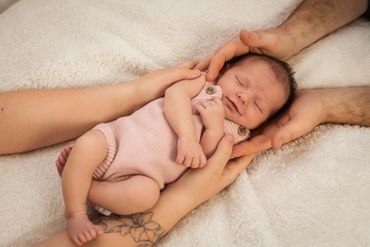 Newborn baby peacefully sleeping in parents' hands on soft blanket.
