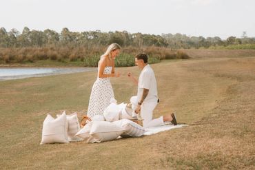 A man proposes to a woman during a romantic outdoor picnic by the lake.