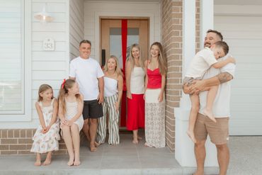 A happy family gathered on a porch with a red ribbon on the door.