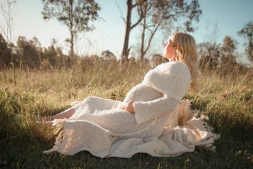 Pregnant woman relaxing outdoors on a blanket in a peaceful field.
