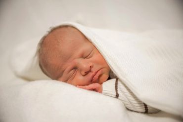 Newborn baby peacefully sleeping wrapped in a white blanket.