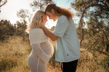 Pregnant woman and partner share a tender moment outdoors.
