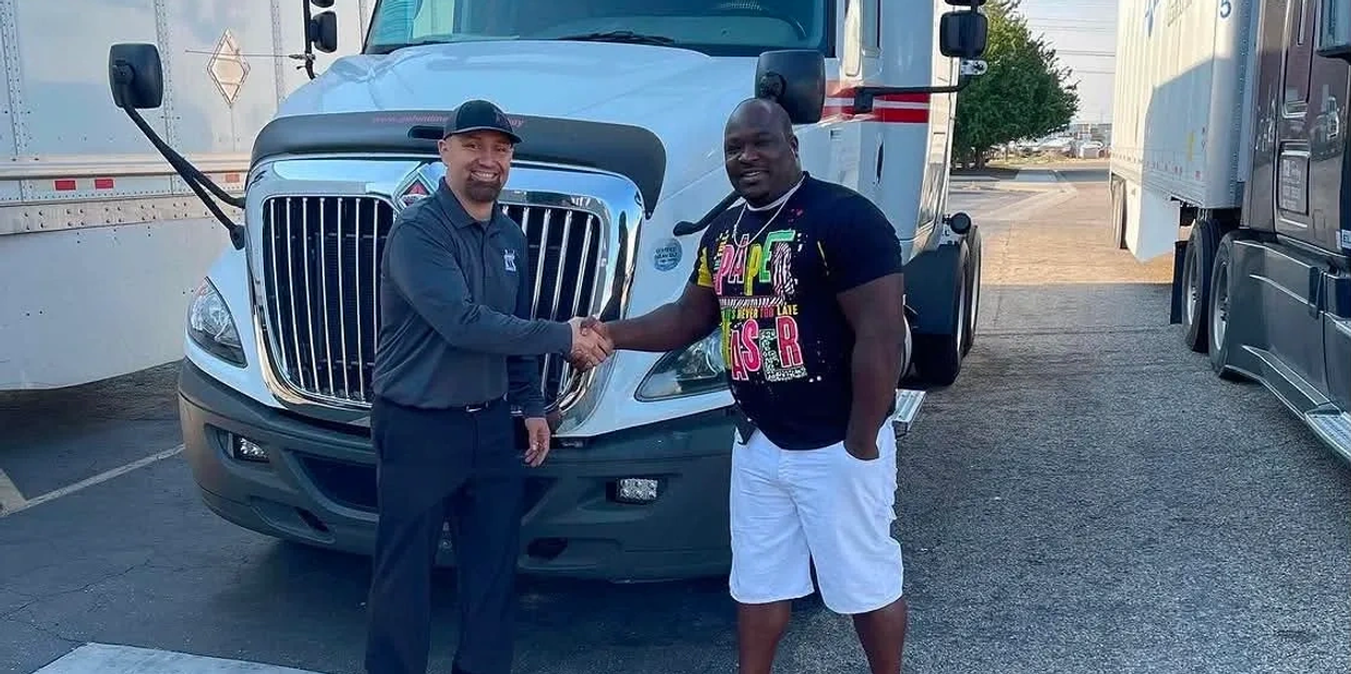 Two men shaking hands in front of a truck.