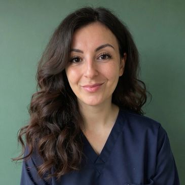 Smiling woman with dark curly hair in navy scrubs against green background.