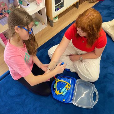 Child and Play therapist, Maddie sitting on the floor. The child is using a doctor kit and bandaging