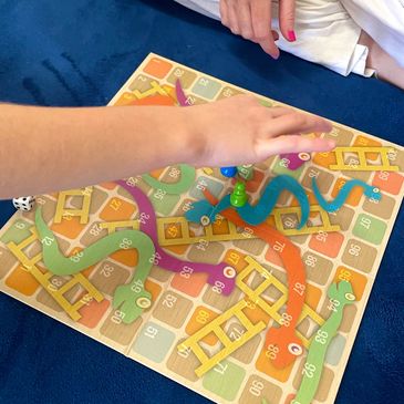 Bird's eye view of snakes and ladders game. A child's hand is moving a piece. 