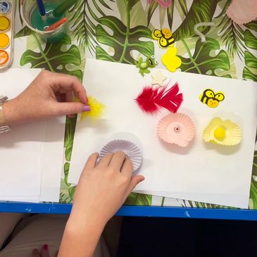 A child and play therapist hand doing craft, using cupcake papers, bees and feathers