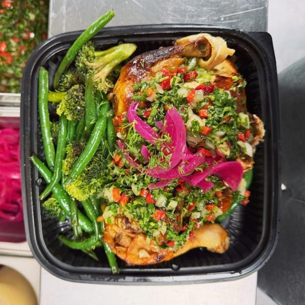 Roasted chicken with green beans, broccoli, and fresh herb garnish in a black container.