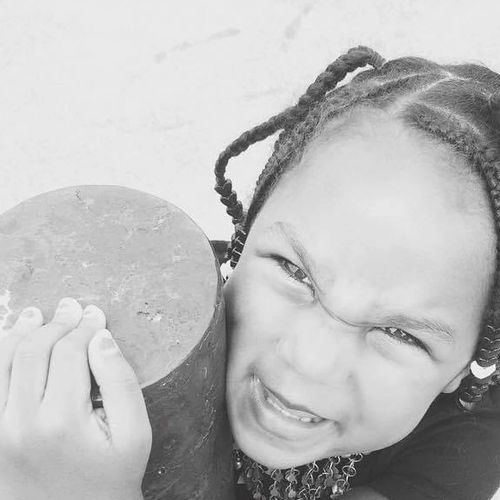 Young girl with braided hair hugging a pole and making a playful face.