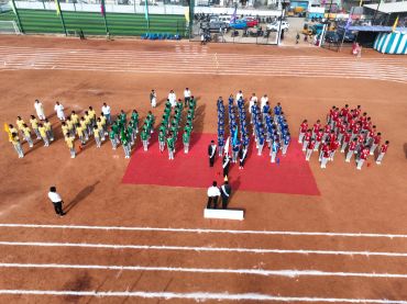 Students lined up on a sports field in red, yellow, green, and blue uniforms.