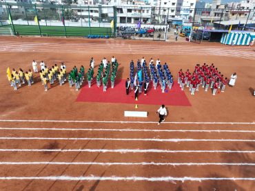 Students in yellow, green, blue, and red uniforms lined up on a sports field.