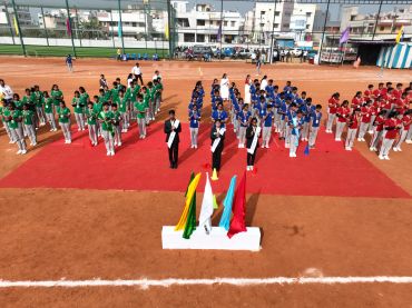 Students assembled on a sports ground in colored uniforms for an event.
