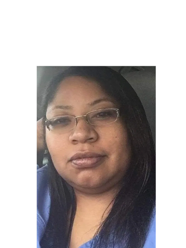 Woman with glasses wearing blue scrubs, sitting in a car.